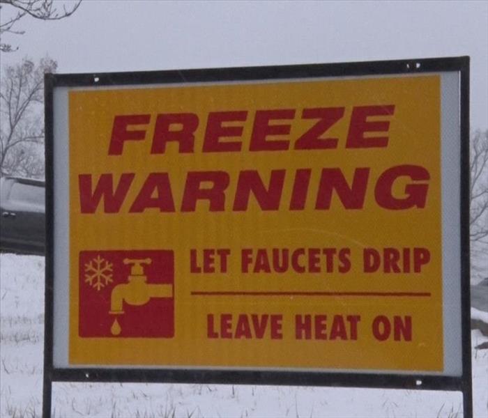 A yard sign with snow in the back on the ground that reads "freeze warning, let faucets drip, leave heat on"