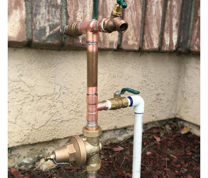 Image of a plumbing set up outside the home with a shut of water valve, house bib, and a water pressure regulator
